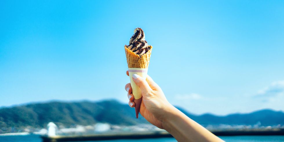 cropped image of woman's hand holding ice cream by the sea against clear blue sky