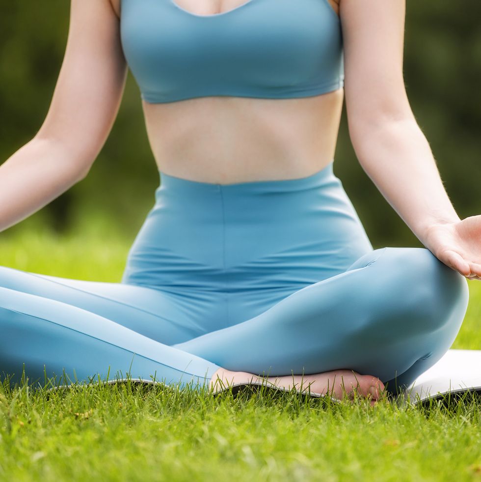 cropped image of young calm woman in sportswear sitting in lotus position outdoors in park