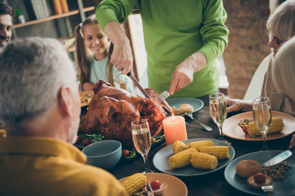 cropped photo of full family sit feast dishes table near roasted turkey grandpa cutting meat into slices hungry relatives waiting excited beginning in living room indoors
