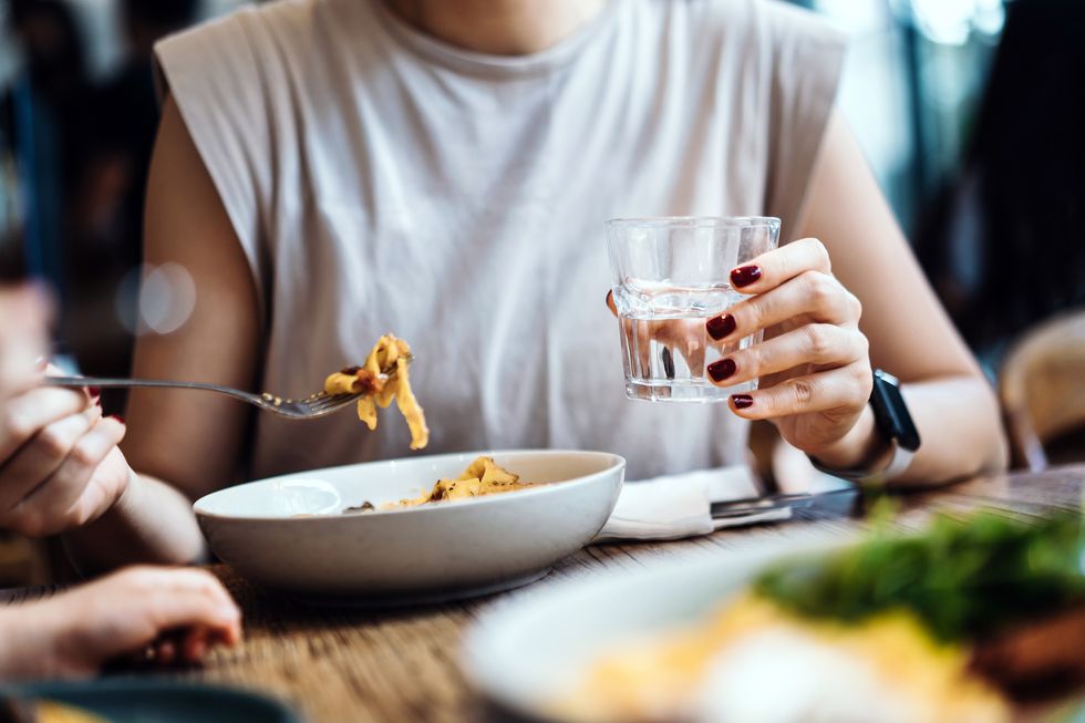 cropped shot of a woman having pasta for lunch in cafe close up of a female eating fresh pasta and drinking a glass of water sitting at dining table people, food and lifestyle concept