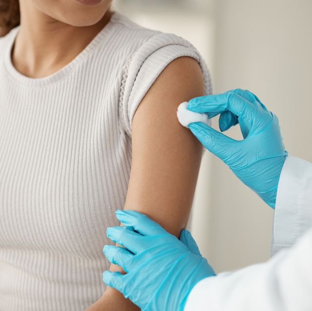 cropped shot of an unrecognisable doctor standing and using a cotton swab on her patient's arm before administering an injection