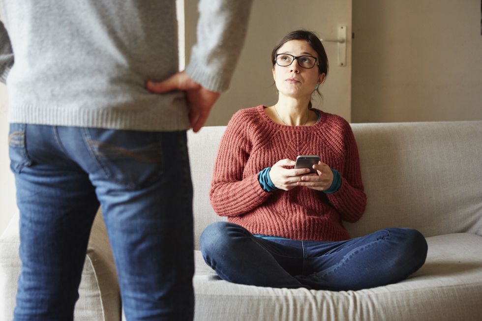 Cropped shot of man in front of girlfriend on sofa with smartphone