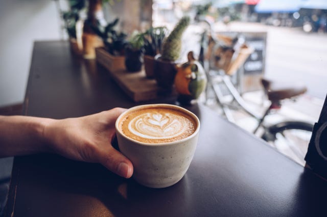 cropped shot of someone hand with a cup of hot latte coffee on the table nearly window