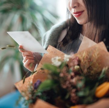 cropped shot of unrecognisable woman reading greeting card attached and holding flower bouquet
