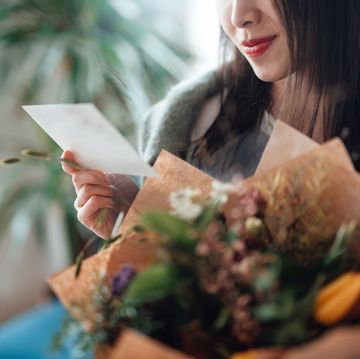 cropped shot of unrecognisable woman reading greeting card attached and holding flower bouquet
