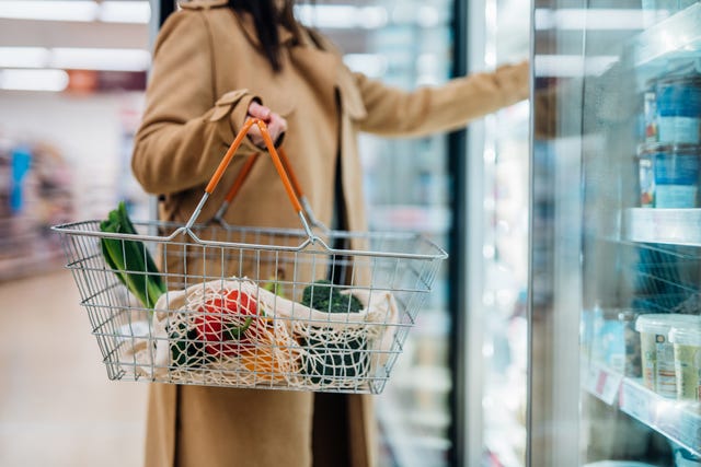 cropped shot of woman carrying shopping basket and standing in front of a cooler case shopping for healthy groceries in supermarket