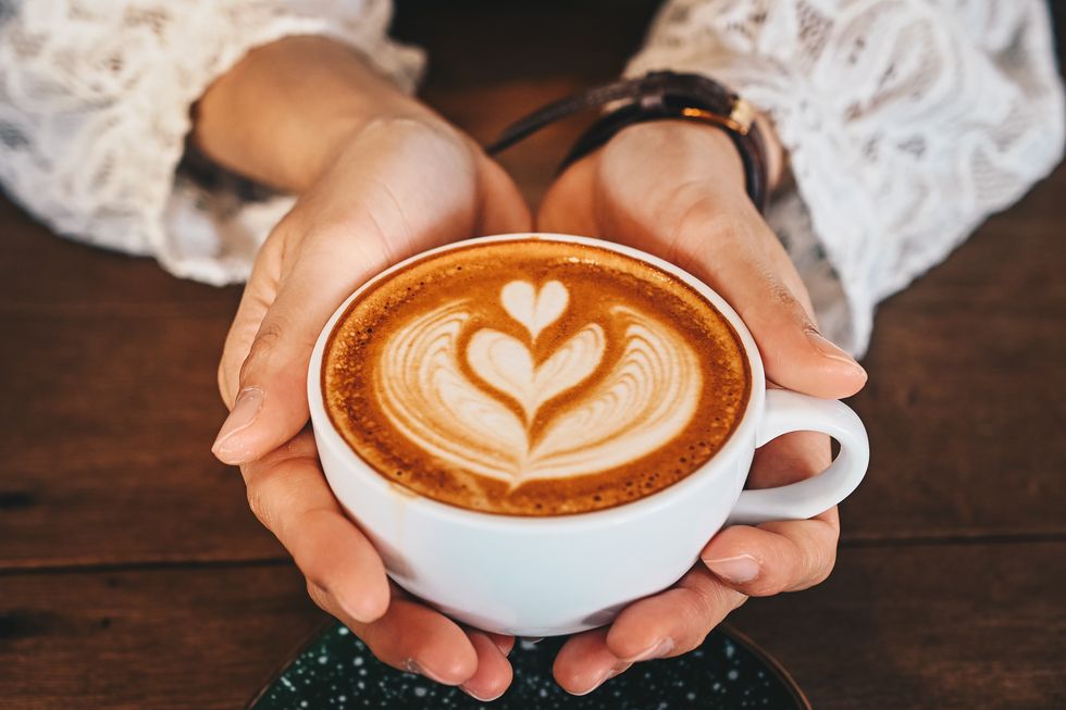 Cropped shot of woman hands holding a cup of hot latte coffee in her hands.