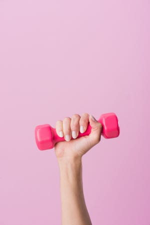 cropped shot of woman holding dumbbell isolated on pink