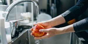 cropped shot of woman's hand washing an red apple with running water in the kitchen sink at home