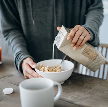 cropped shot of young asian mother preparing healthy breakfast, pouring milk over cereals on the kitchen counter