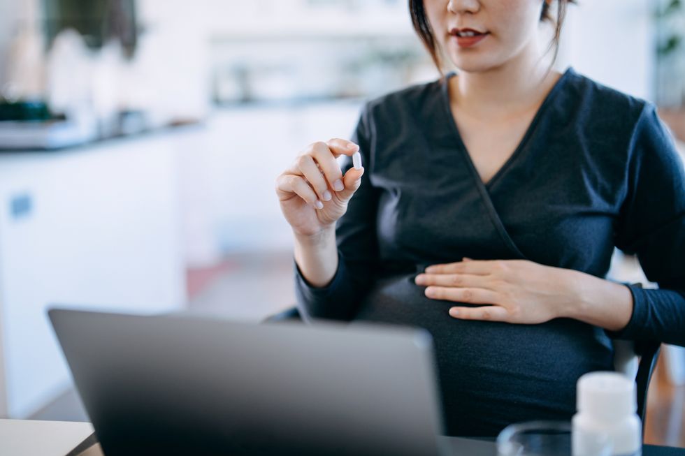cropped shot of young asian pregnant woman holding medicine on hand, having video call with doctor using laptop at home, consulting on medication telemedicine during pregnancy pregnancy health and wellness concept