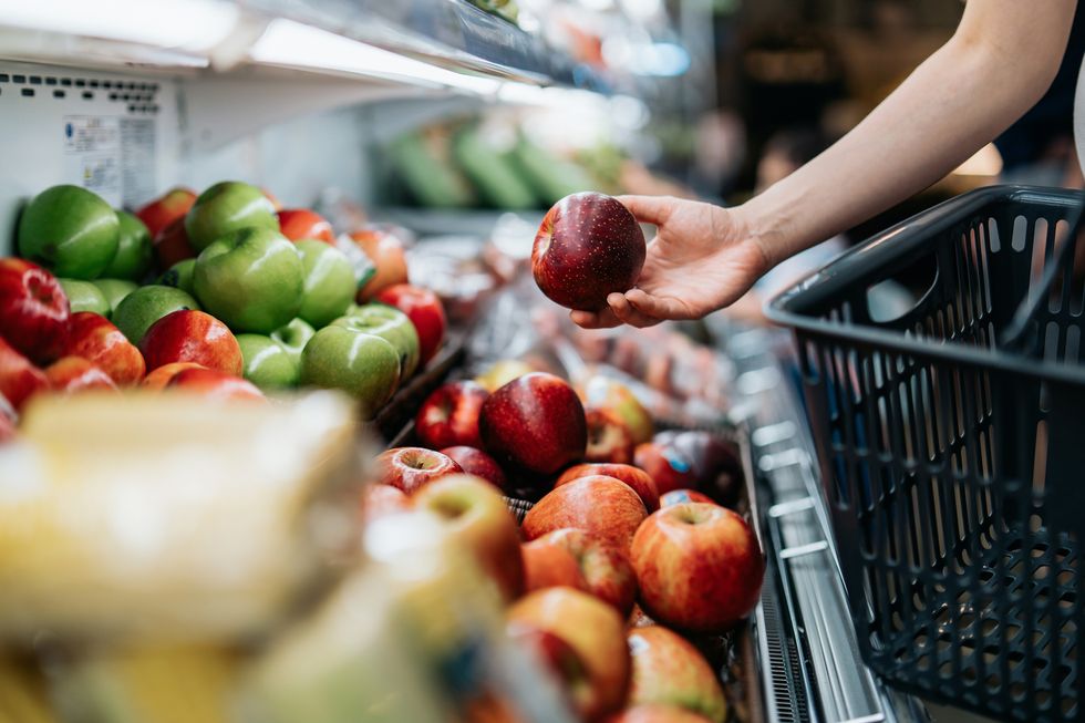 cropped shot of young asian woman choosing fresh organic fruits in supermarket she is picking a red apple along the produce aisle routine grocery shopping healthy living and eating lifestyle
