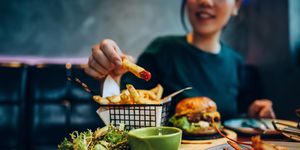 cropped shot of young asian woman eating freshly made delicious burger, dipping fries in ketchup on the dining table enjoying a feast in the restaurant people, food and lifestyle
