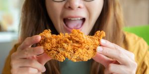 cropped shot of young asian woman open her mouth before eating a piece of crispy fried chicken
