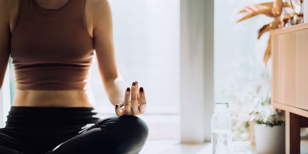 cropped shot of young asian woman sitting on the exercise mat, meditating in the lotus pose during a yoga session at home in the fresh bright morning fitness, wellness and home work out concept