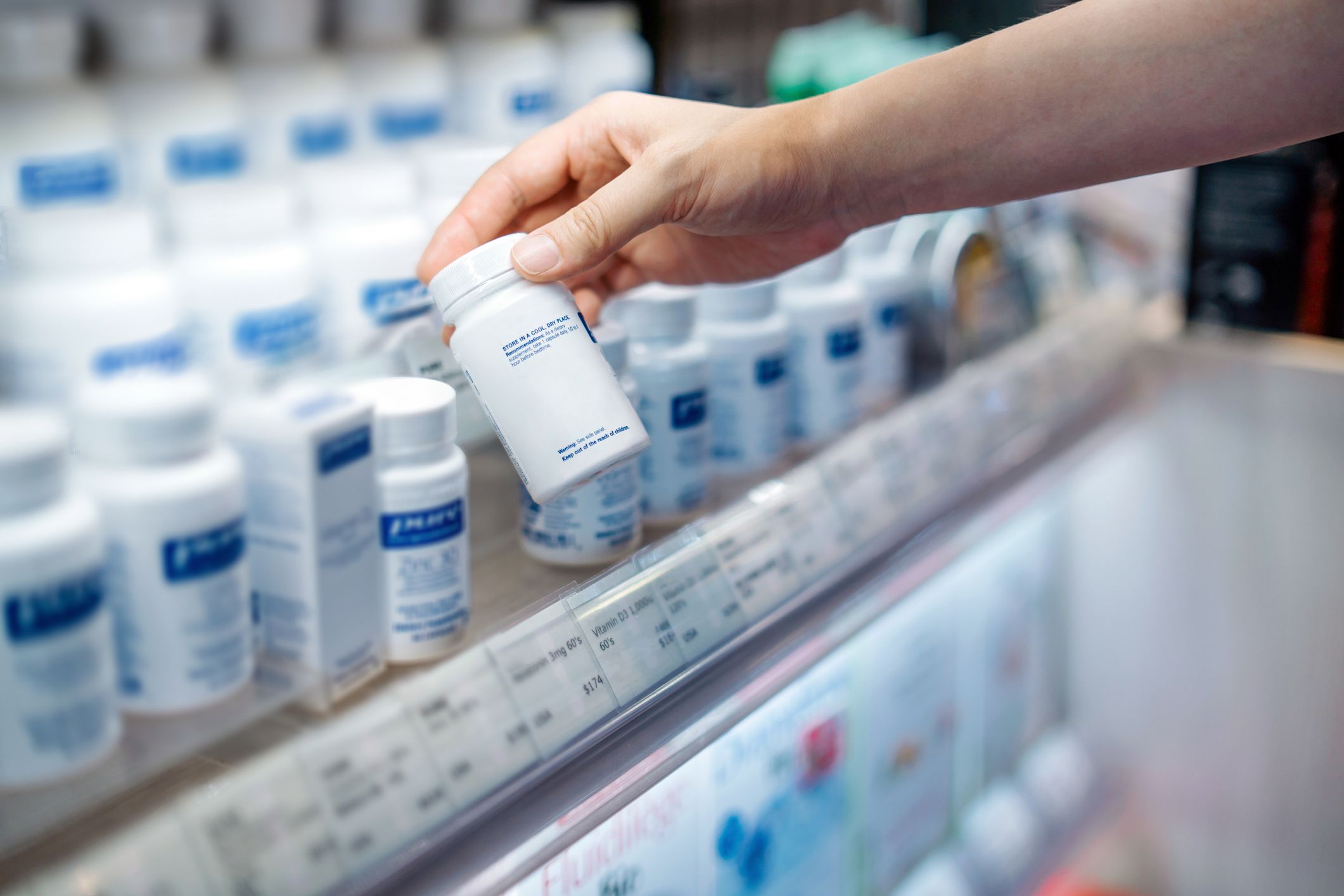cropped shot of young asian woman's hand taking a bottle of medicine from the shelf at the pharmacy, reading the product information healthcare, medication and people concept