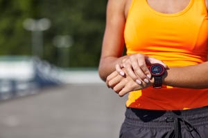 cropped shot of young female runner setting smartwatch in parking lot