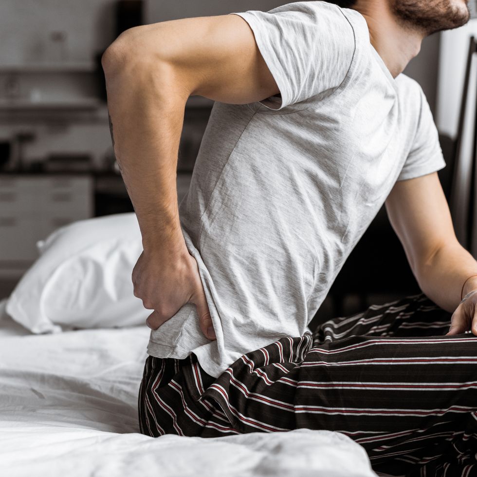 a man massages his lower back while sitting in bed