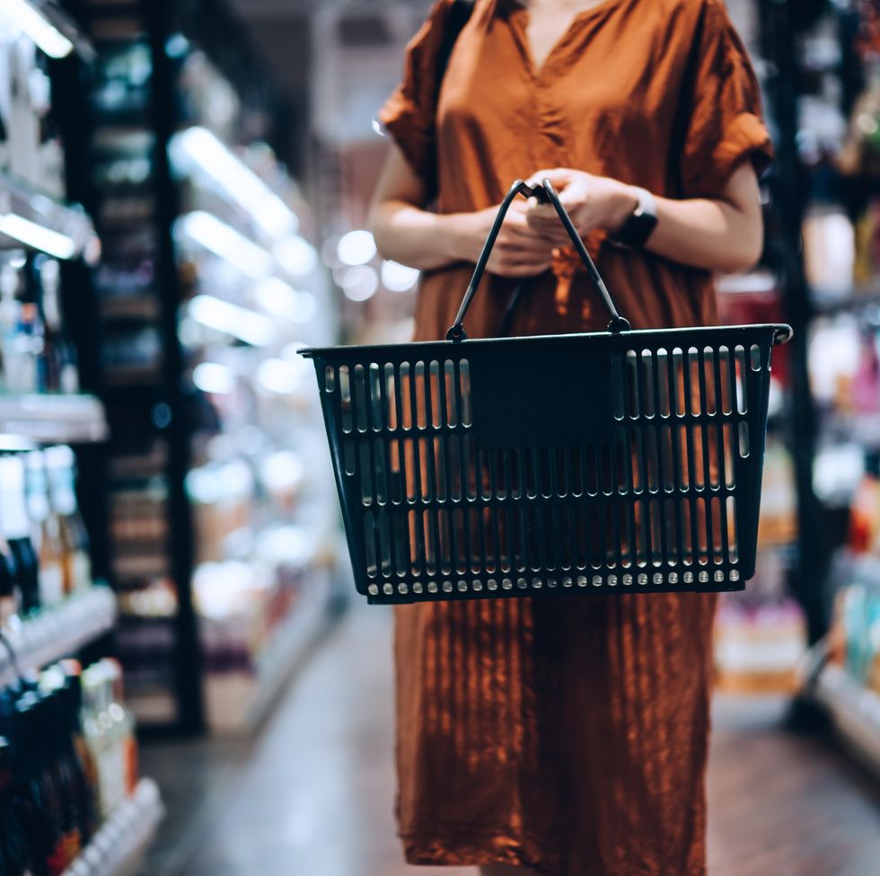 cropped shot of young woman carrying a shopping basket, standing along the product aisle, grocery shopping for daily necessities in supermarket
