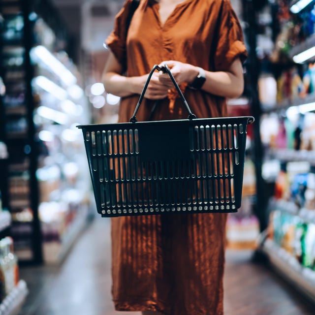 cropped shot of young woman carrying a shopping basket, standing along the product aisle, grocery shopping for daily necessities in supermarket