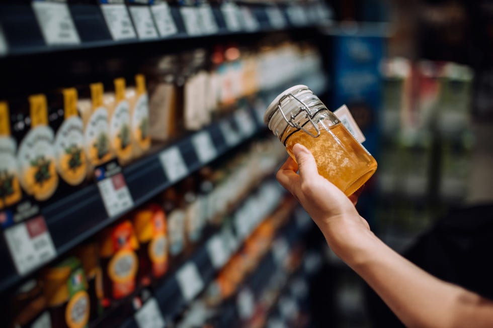 cropped shot of young woman shopping in supermarket, taking bottle of organic honey from produce aisle and reading nutrition label on bottle routine shopping healthy food lifestyle