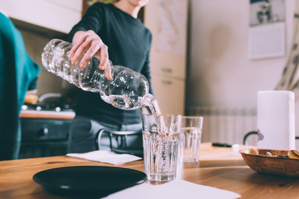 cropped shot of young woman pouring water at kitchen table