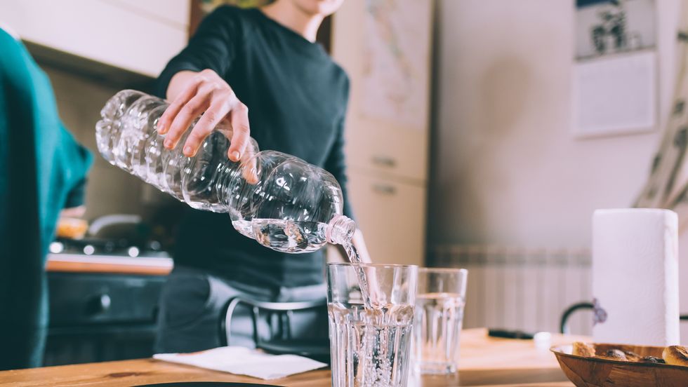 Cropped shot of young woman pouring water at kitchen table