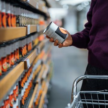 cropped shot of young woman pushing a shopping cart, grocery shopping in supermarket. she is holding a tin can and reading the nutritional label. routine grocery shopping. food shopping. making healthier food choices