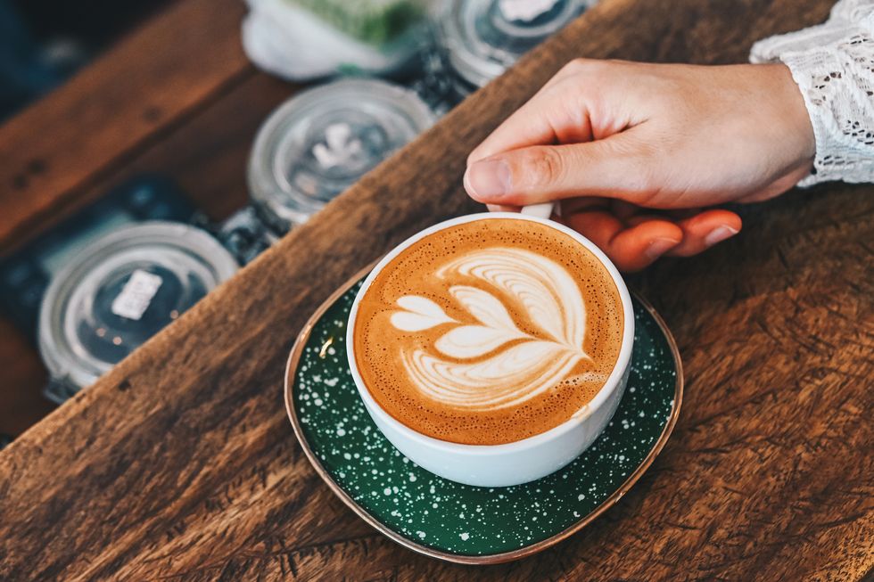 cropped shot view of woman hand touching a cup of hot latte coffee on the wooden table