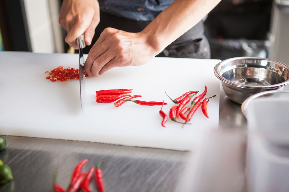 cropped view of man slicing red chilli peppers