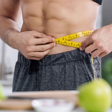 cropped view of shirtless man measuring waist near nutritious food