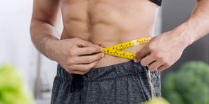 cropped view of shirtless man measuring waist near nutritious food