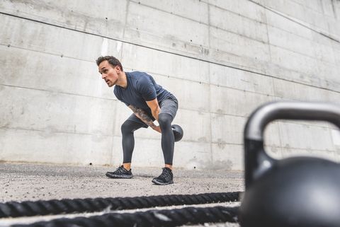 crouching male athlete doing double handed kettlebell swing