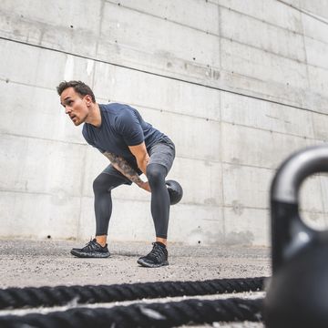 crouching male athlete doing double handed kettlebell swing