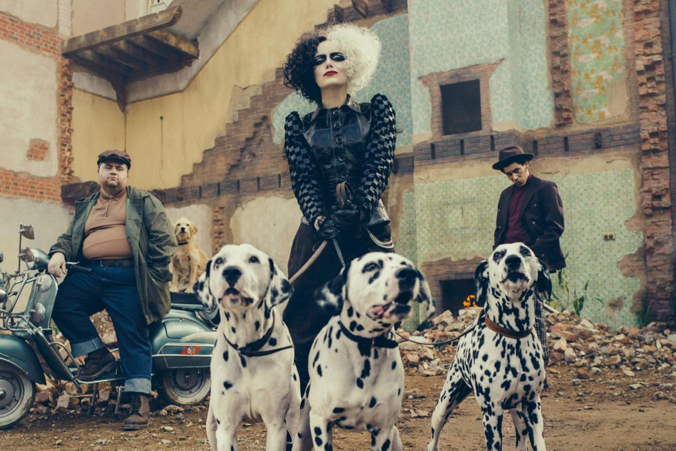 emma stone as cruella holding dalmatian dogs, cruella