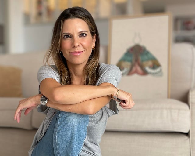 artista laura zambrana sentada en el suelo con un cuadro de mariposas detras