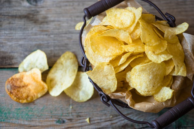 bodegón de patatas fritas de bolsa en una cesta y extendida sobre la mesa un claro ejemplo de comida procesada
