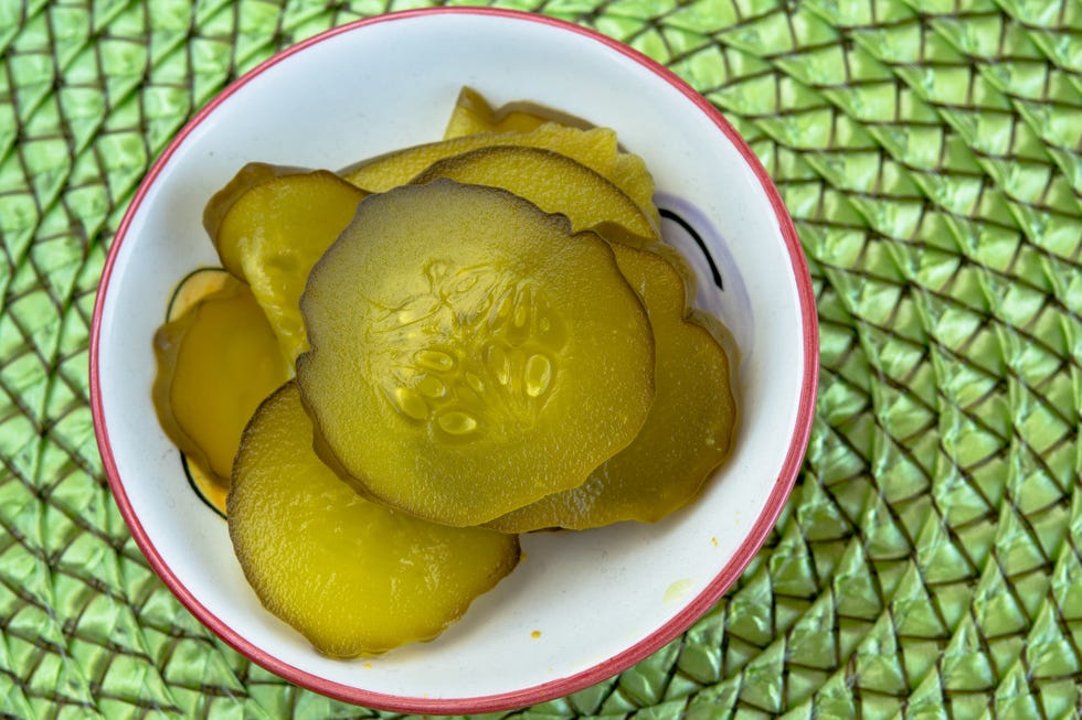 cucumber pickles served on a white small bowl and over a green textured background