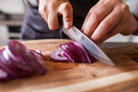 hands cutting a red onion with a knife