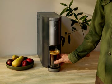 coffee maker with a hand pouring coffee into a glass surrounded by fruits