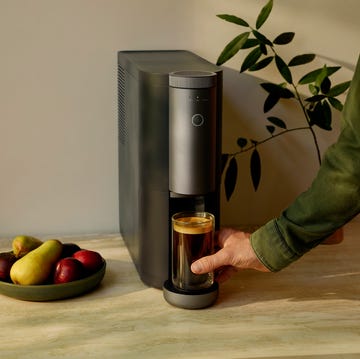Cumulus Coffee Maker coffee maker with a hand pouring coffee into a glass surrounded by fruits