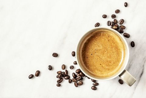 A cup of coffee and coffee beans on white, marble background