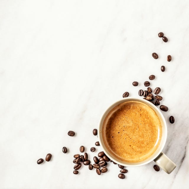 a cup of coffee and coffee beans on white, marble background
