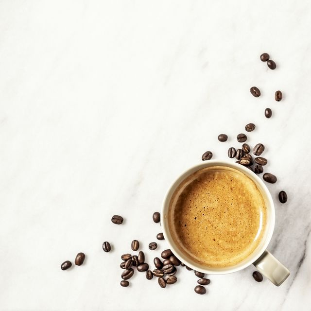 a cup of coffee and coffee beans on white, marble background