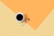 coffee in white coffee cup on a white saucer with metal spoon on an orange and yellow background, giving up coffee for lent