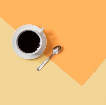 coffee in white coffee cup on a white saucer with metal spoon on an orange and yellow background, giving up coffee for lent