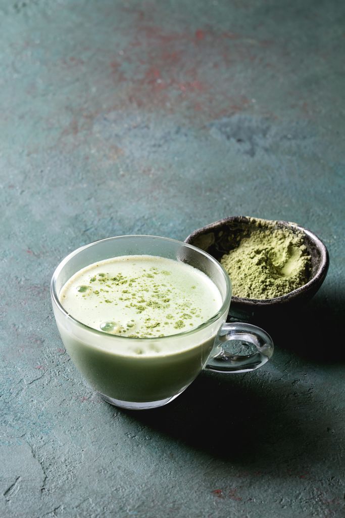 cup of matcha latte with bowl of matcha tea over grey green texture background copy space