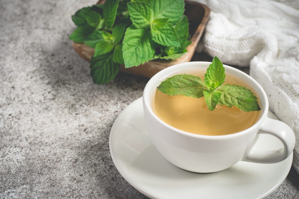 cup of mint tea closeup, fresh mint leaves and a rug on a gray background