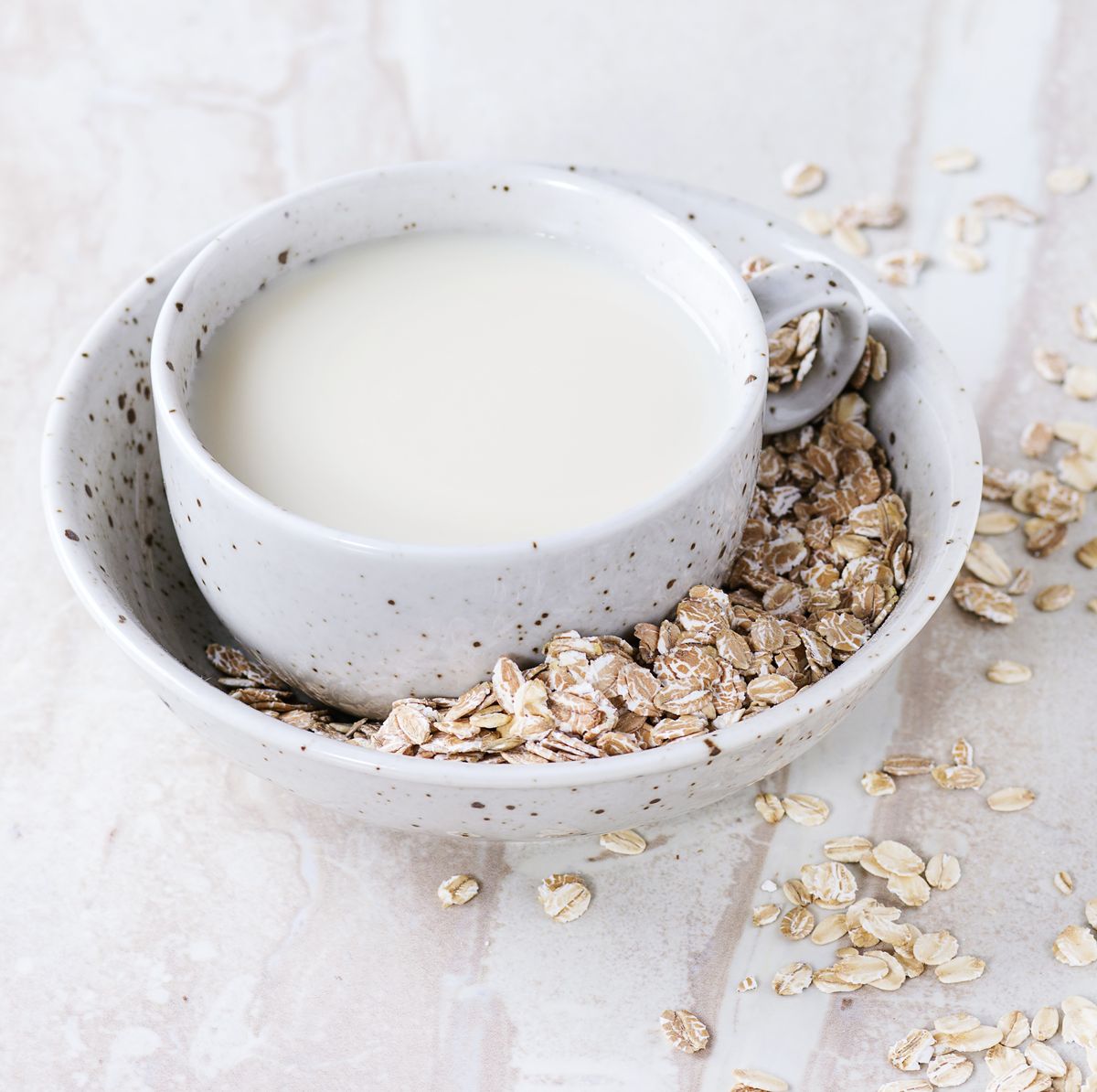 A cup of oat milk in bowl of oats on a marble surface
