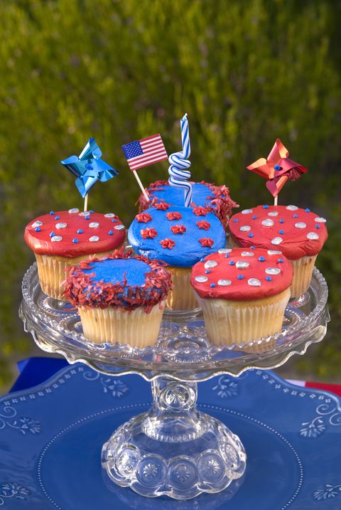 six red or blue decorated cupcakes on a cut glass cake stand